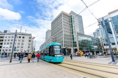 Frankfurt, Germany - October 21, 2025: Modern turquoise tram traverses a vibrant urban intersection in Frankfurt, Germany, flanked by contemporary architectural structures and active pedestrian
