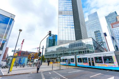 Frankfurt, Almanya - 21 Ekim 2025: Arkasında uzun gökdelenler bulunan bir tramvay istasyonunun yanındaki caddeyi geçen yaya