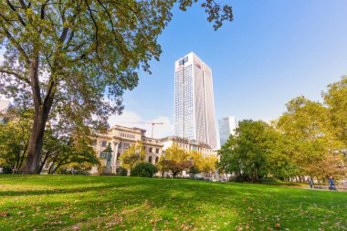Frankfurt, Germany - October 21, 2025: Prominent skyscraper with a visible UBS logo dominates Frankfurt's financial district, overlooking a tranquil urban park with autumnal trees.