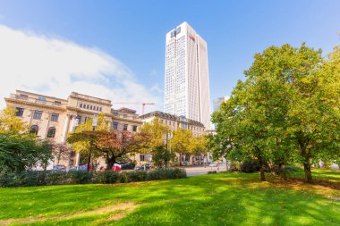 Frankfurt, Germany - October 21, 2025: Urban landscape showcases a striking modern skyscraper juxtaposed with classical buildings, framed by a vibrant green park in Frankfurt.