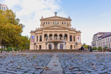 Frankfurt, Almanya - 21 Ekim 2025: Iconic Alte Oper binası soğuk bir sonbahar gününde gururla ayakta duruyor, neoklasik cephesi merkezi bir çeşme ve yapraklarla süslenmiş bir plazayla tamamlanmış.