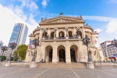Frankfurt, Almanya - 21 Ekim 2025 Frankfurt 'un büyük Eski Opera Binası mavi gökyüzünün altında duruyor. Bisikletli bir kişi adımlarına bağlı, tarihi kentsel modernlikle harmanlıyor..