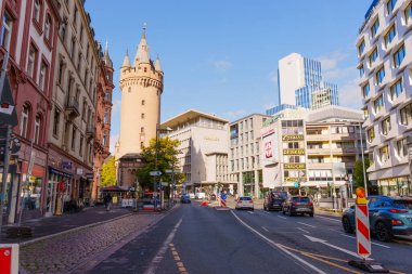 Frankfurt, Almanya - 21 Ekim 2025: Frankfurt 'un hareketli kentsel caddesi tarihi Eschenheimer Kulesi, modern yapılar ve açık mavi gökyüzü altında hareket eden arabaları barındırıyor.