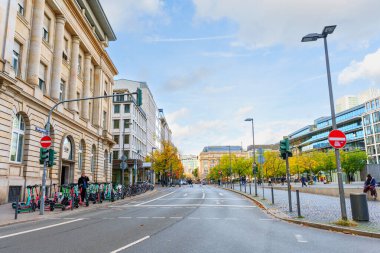 Frankfurt, Germany - October 21, 2025: Frankfurt's urban street features historic architecture, modern buildings, parked electric scooters, and autumn trees under a bright blue sky on a clear day.