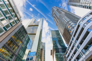 Frankfurt, Almanya - 21 Ekim 2025: Frankfurt 'un çağdaş cam gökdelenleri beyaz bulutlarla mavi gökyüzünü delip, şehrin modern finans bölgesini gündüz göstermektedir.