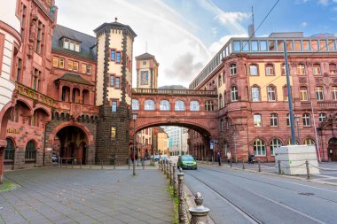 Frankfurt, Almanya - 21 Ekim 2025: Frankfurt 'un tarihi kırmızı kumtaşı belediye binası aydınlık bir günde tramvay raylarıyla bir cadde üzerinde iki binayı birbirine bağlayan kemerli bir gökdeleni içeriyor