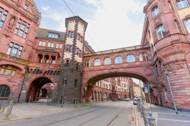 Frankfurt, Almanya - 21 Ekim 2025: Frankfurt 'un tarihi kırmızı kumtaşı belediye binası, üzerinde tramvay rayları bulunan bir cadde boyunca uzanan süslü yaya köprüsü, parlak bir günde göze çarpıyor..