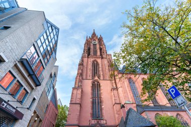 Frankfurt, Almanya - 21 Ekim 2025: Görkemli Gotik Katedral Kulesi, Frankfurt 'taki açık mavi gökyüzü altında çağdaş binalar ve canlı sonbahar yaprakları arasında belirgin bir şekilde yükseliyor.
