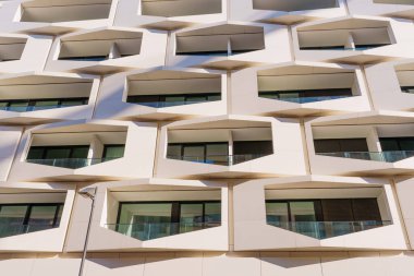 Çağdaş bir binanın dış cephesinin mimari harikası geometrik balkonlara ve tenha pencerelere çarpar. Güneş ışığı güçlü gölgeler yaratır, modern, tekrarlayan tasarımı vurgular..