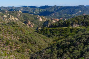 Güneşli yemyeşil tepeler ve dramatik kırmızı kaya oluşumları Kaliforniya 'nın Santa Monica Dağları' ndaki Red Rock Kanyon Parkı 'nın genişleyen güzelliğini karakterize etmektedir..
