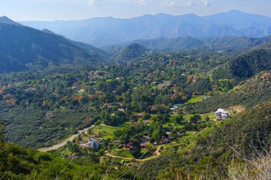 Kızıl Kaya Kanyonu Parkı vadisinde dağınık konut yapıları ve virajlı yollar yer almakta, engebeli Santa Monica Dağları arasında berrak mavi bir gökyüzünün altında..