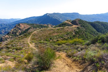 Çamurlu yollar çorak, fırçayla kaplı tepeler, bulutsuz gökyüzünün altında Santa Monica Dağları, Red Rock Kanyon Parkı 'ndaki görkemli dağlara doğru ilerliyor..