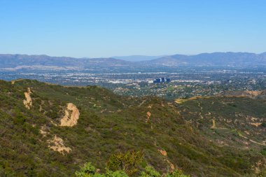 Santa Monica Dağları 'ndaki Red Rock Kanyon Parkı' nın geniş manzarası açık mavi gökyüzünün altındaki Los Angeles Havzası 'na bakan kaya oluşumlarıyla dolu yeşil tepeler sergiliyor..