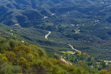 Santa Monica Dağları 'ndaki Red Rock Kanyon Parkı' nın yoğun bitki örtüsü içinde kıvrımlı yol yılanları dağınık evlerle dolu parlak bir sonbahar gününde.