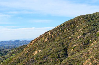 Chaparral kaplı yamaçlar ve parlak mavi gökyüzünün altında belirgin kaya oluşumları Red Rock Canyon Park, Santa Monica Dağları 'nın doğal güzelliklerini gözler önüne seriyor..