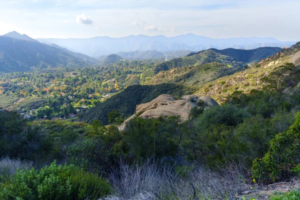 Kızıl Kaya Kanyon Parkı 'ndaki yemyeşil vadi yoğun ağaçlar ve belirgin kaya oluşumları arasında Santa Monica Dağları' na kadar uzanan dağınık evler sergiliyor..