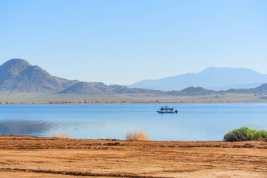 Perris Gölü 'nün sakin mavi sularında, engebeli dağlar ve parlak, berrak bir gökyüzünün altındaki kuru toprak çerçevesinde iki kişiyle birlikte yol alıyoruz..
