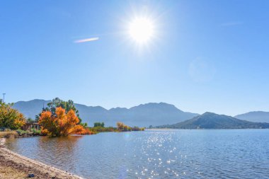 Parlak sonbahar yaprakları Perris Gölü 'nün ışıl ışıl sularını çevreleyerek berrak mavi gökyüzünün altındaki uzak puslu dağlara karşı parlak güneş ışığını yansıtır..