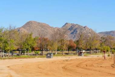 Perris Gölü 'nün piknik alanı ve tozlu arazisi üzerinde dağlar yükseliyor. Ağaçlar açık mavi gökyüzü altında sonbahar renklerini gösteriyor..