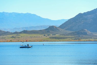 Ziyaretçiler, berrak bir gökyüzünün altındaki engebeli dağlar tarafından çerçevelenmiş Perris Gölü 'nün sakin ve mavi sularında kayıkla gezmenin keyfini çıkarıyorlar..
