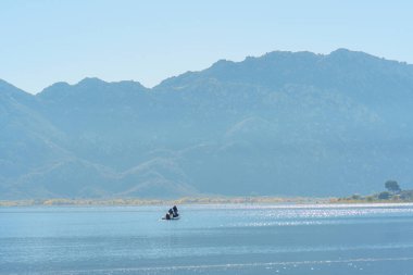 İki insan, Perris Gölü 'nün güneşli yüzeyinde süzülen küçük bir teknede huzurlu bir günün tadını çıkarıyor..