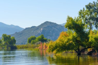 Bereketli yeşil ve altın ağaçlar Perris Gölü 'nün sakin sularında berrak mavi gökyüzünün altında engebeli dağlar, huzurlu bir doğal manzara yaratıyor..