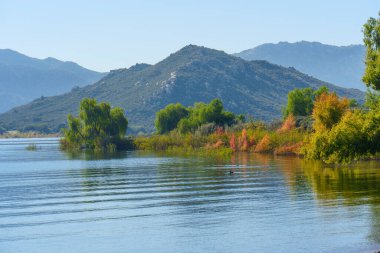Titrek düşen yapraklar Perris Gölü 'nün sakin sularını berrak bir gökyüzü altında, sakin doğal bir zemin sağlayan uzak dağları oluşturur..