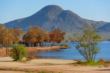Parlak, berrak bir gökyüzünün altında heybetli kayalık bir dağ sunan Perris Gölü 'nün sakin mavi sularını güzel bir şekilde çevreleyen canlı sonbahar yaprakları..