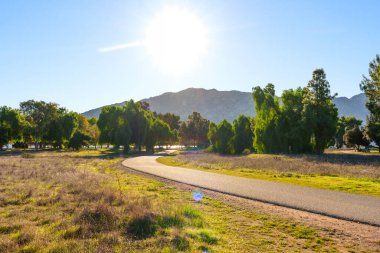 Asfalt dolambaçlı yol yeşil ağaçların ve kuru otların arasından uzak dağlara, Perris Gölü 'nde güneşli bir gökyüzünün altına uzanır..