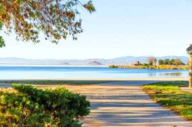 Perris Gölü Eyalet Dinlenme Alanı 'nın sakin suları açık bir gökyüzünün altında uzak dağlarla buluşur. Davetkar bir yol huzur veren doğal güzelliklere götürür..