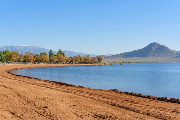 Perris 'in sakin göl suları, kıvrımlı kumlu bir sahil, renkli sonbahar ağaçları ve görkemli uzak dağlarla çevrili berrak mavi bir gökyüzünü yansıtır..