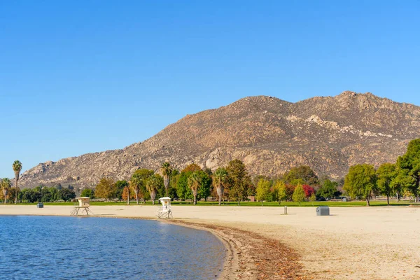 Perris Gölü 'nde güneşli bir gün. Huzurlu suları, kumlu plajı, iki cankurtaran standı, canlı ağaçlar ve yüksek bir kayalık dağ..