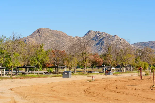 Perris Gölü 'nün piknik alanı ve tozlu arazisi üzerinde dağlar yükseliyor. Ağaçlar açık mavi gökyüzü altında sonbahar renklerini gösteriyor..