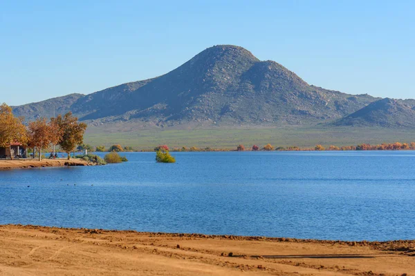 Perris Gölü 'nün mavi suları, engebeli dağlar ve açık bir gökyüzünün altında uzak kıyı boyunca renkli sonbahar ağaçları tarafından destekleniyor..