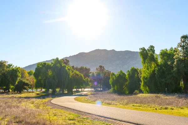 Dolambaçlı asfalt yol, güneşli yeşil ağaçlar ve kuru otlar arasından Perris Gölü 'nün açık mavi gökyüzünün altındaki uzak bir dağa, aydınlık bir günde uzanır..
