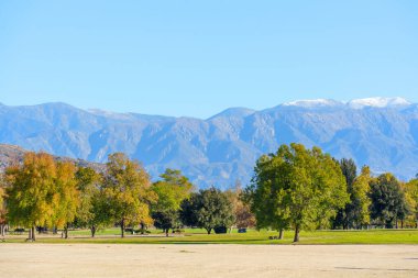 Renkli sonbahar yeşillikleri, Perris Gölü 'ndeki görkemli, karla kaplı dağların altındaki yeşil bir parkı çerçeveler..