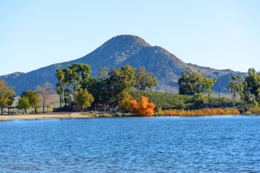 Perris Gölü 'nün engin mavi suları engebeli bir dağa karşı canlı sonbahar renklerini gösteren ağaçlarla kaplı manzaralı bir kıyı şeridiyle karşılaşıyor..