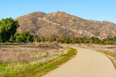 Berrak mavi gökyüzünün altındaki engebeli bir dağa uzanan, güneşten sırılsıklam olmuş çimen tarlaları boyunca esiyor. Perris Eyaleti Dinlenme Bölgesi 'nin karakteristik bir özelliği..