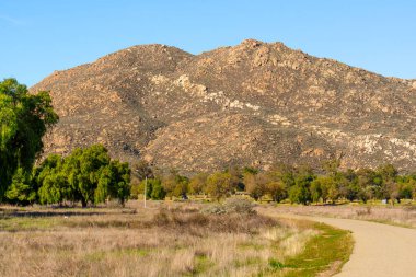 Engebeli, kayalarla kaplı dağ, kıvrımlı bir patika, yeşil ağaçlar ve parlak gök kubbenin altında güneşte kavrulmuş otlaklar..