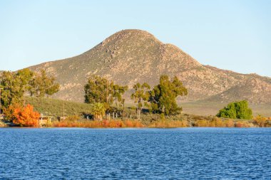 Perris Gölü 'nün geniş mavi suları berrak bir gökyüzünün altında dalgalanır. Ağaçlarla kaplı çeşitli bir kıyı büyük kayalıklara, bitkilerle kaplı bir dağa çıkar..