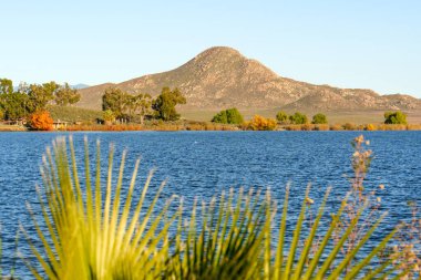 Berrak mavi gökyüzünü yansıtan Perris Gölü 'nün sakin suları canlı sonbahar ağaçları ve engebeli dağlarla çevrili..
