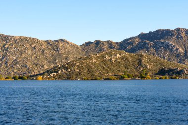 Perris Gölü 'nün derin mavi suları geniş, güneşli dağların altında yavaşça dalgalanır kayalık özellikler ve esnek çalılıklarla süslenir..