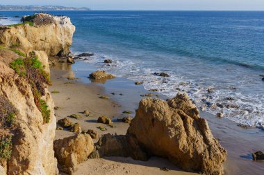 Rugged sea stacks and expansive sandy beach define El Matador State Beach in Malibu, with tranquil ocean waves gently meeting the shore under a bright sky.