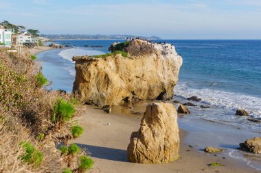 Expansive view of El Matador State Beach, Malibu, California, with rugged sea stacks, sandy shores, and vibrant blue Pacific Ocean waters under a clear sky.