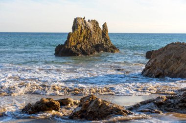 Okyanustan dramatik deniz yığınları yükseliyor, köpüklü dalgalar Malibu, Kaliforniya 'daki kumlu El Matador Eyalet Sahili' ne vuruyor..