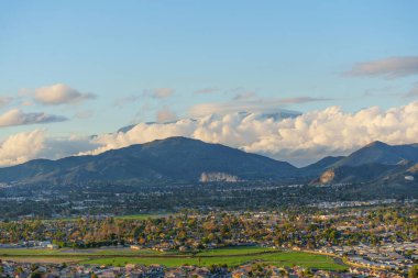 Riverside, Kaliforniya 'nın yerleşim alanları ve yeşil alanlar altın saat ışığıyla aydınlatılmış görkemli bir dağ sırasına doğru uzanıyor..