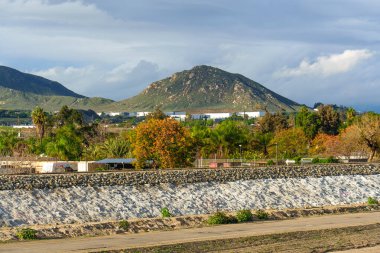 Riverside, Kaliforniya 'nın Rubidoux Dağı' nın manzaralı manzarası, bir demiryolu hattı, ve bulutlu bir gökyüzünün altında canlı sonbahar ağaçları, doğayla gelişimi harmanlıyor..
