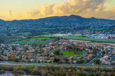 Kenar mahallelerin, yeşil parkların ve yerel havalimanının bulunduğu Riverside California şehri Rubidoux Dağı yakınlarında dramatik bir altın gün batımı gökyüzü altında..
