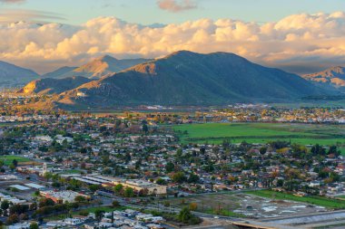 Kaliforniya 'daki Rubidoux Dağı Patikası' ndan dramatik bulutlu bir gökyüzünün altındaki yerleşim yerlerine ve sıradağlara bakan altın saat manzaralı nehir kenti..