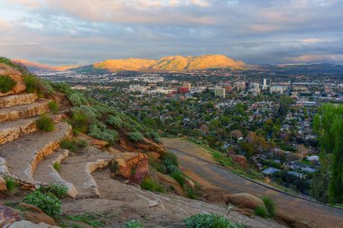 Rubidoux Dağı 'ndan yayılan panorama, bulutlu bir gökyüzü altında güneşli dağlara doğru uzanan Riverside, California' yı kaplıyor..